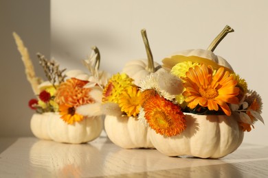 Photo of Small pumpkins with beautiful flowers and spikelets on white wooden table, closeup