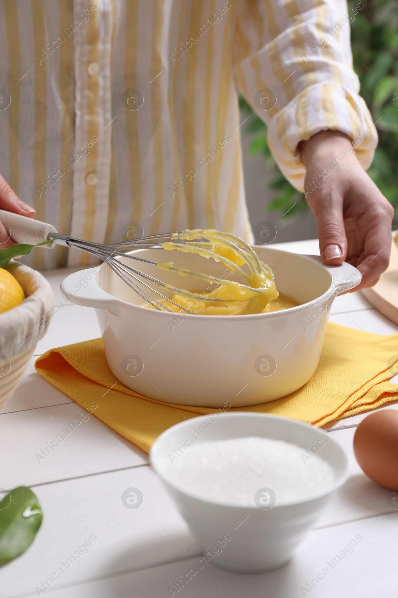 Photo of Woman cooking lemon curd at white wooden table, closeup