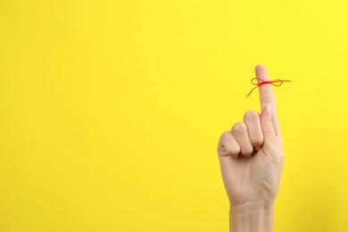 Photo of Woman showing index finger with tied red bow as reminder on yellow background, closeup. Space for text