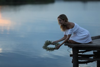 Young woman putting wreath made of beautiful flowers in water