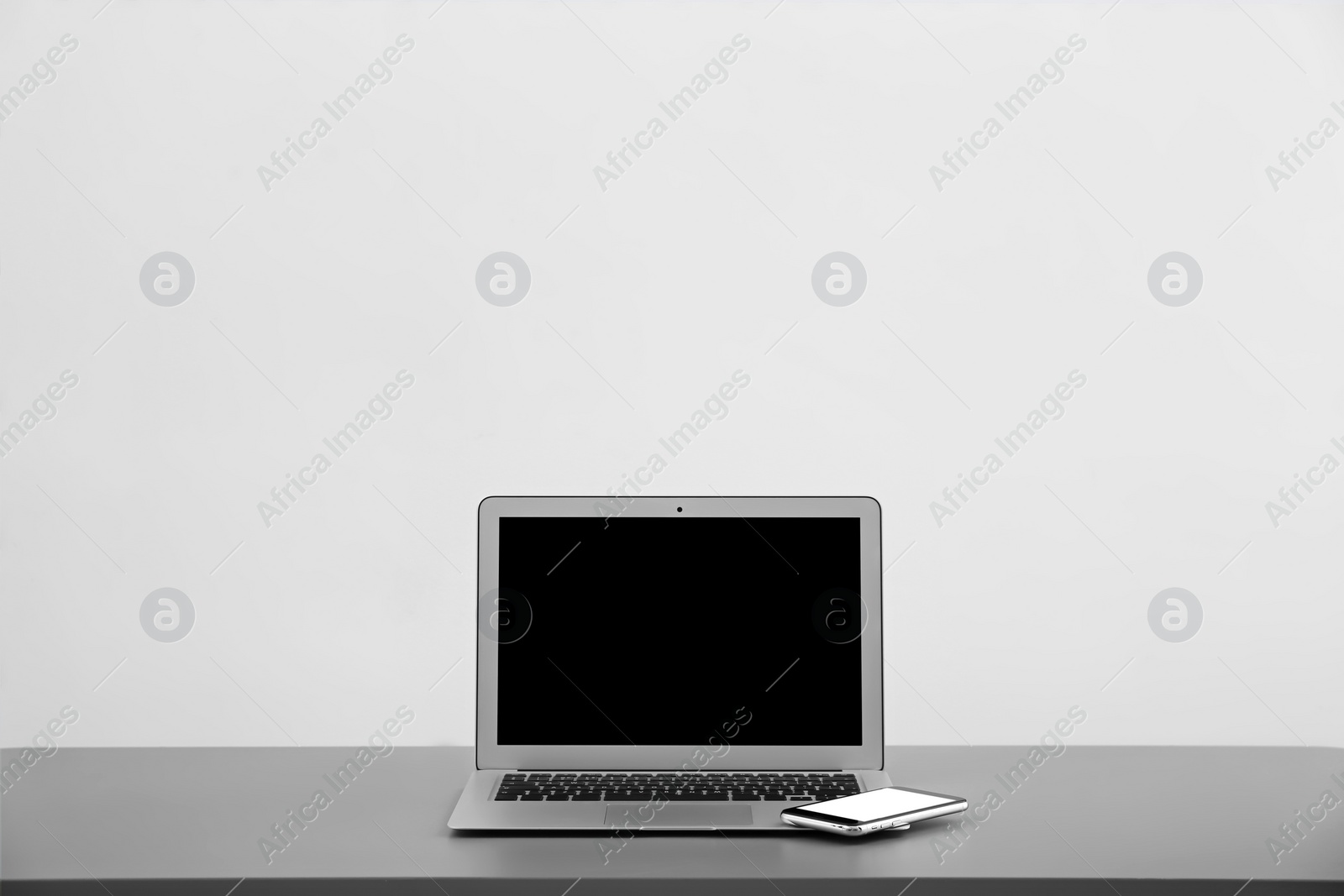 Photo of Modern laptop with blank screen and mobile phone on table against light background