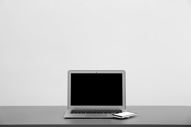 Photo of Modern laptop with blank screen and mobile phone on table against light background