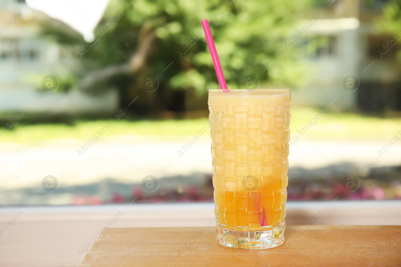 Photo of Glass with delicious cocktail on table against blurred background