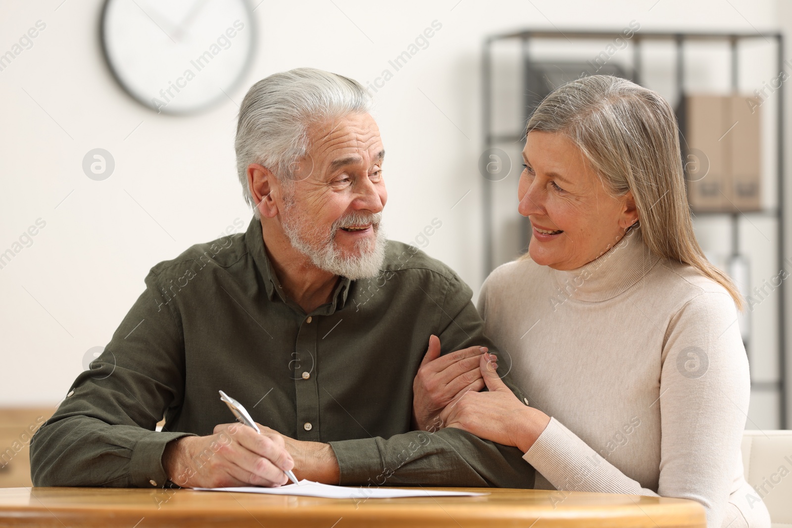 Photo of Happy senior couple signing Last Will and Testament indoors