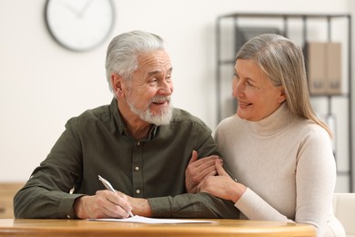 Happy senior couple signing Last Will and Testament indoors