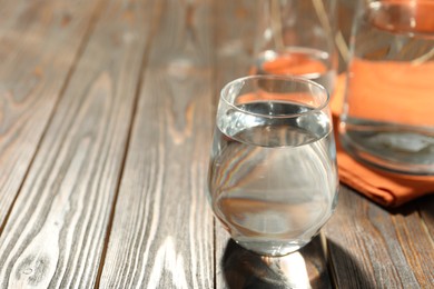 Glass of water on wooden table, space for text. Refreshing drink