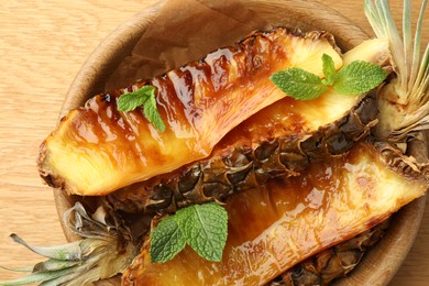 Tasty grilled pineapples in bowl on wooden table, top view