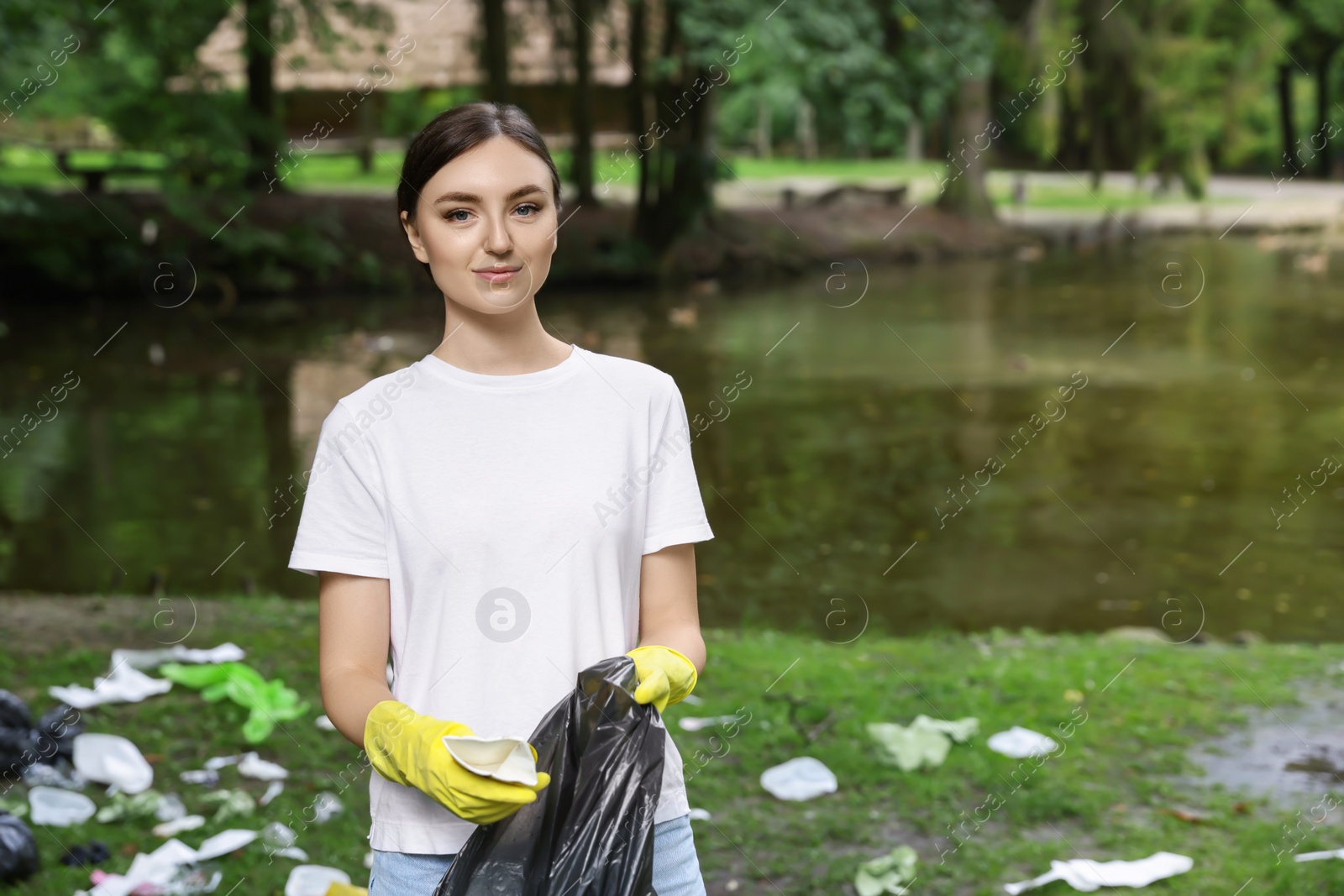 Photo of Young woman with plastic bag collecting garbage in park