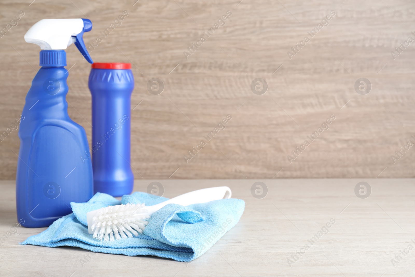 Photo of Microfiber cloth, brush and detergents on white wooden table. Space for text