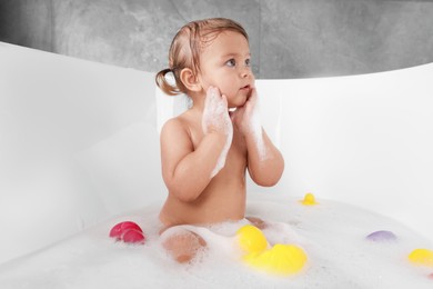 Cute little girl taking bubble bath with toys indoors