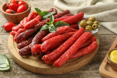 Photo of Different thin dry smoked sausages, basil and olives on wooden table, closeup