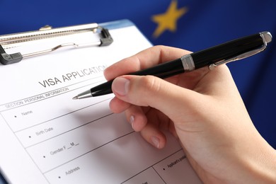 Photo of Woman filling visa application form against flag of European Union, closeup