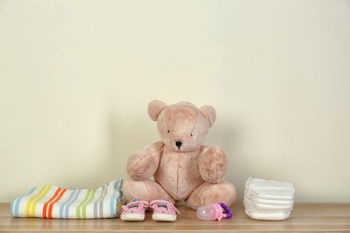 Teddy bear and baby accessories for nursery room interior on wooden table near light wall