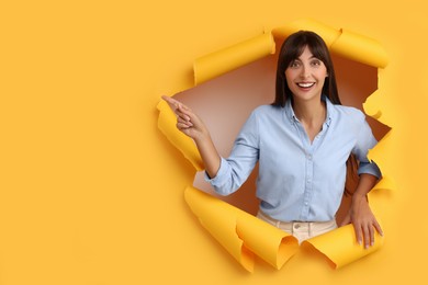 Photo of Special promotion. Woman pointing at something through hole in orange paper. Space for text