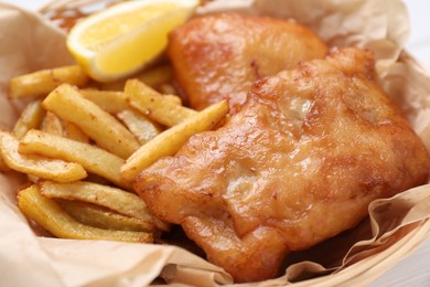 Photo of Tasty fish, chips and lemon in wicker bowl, closeup