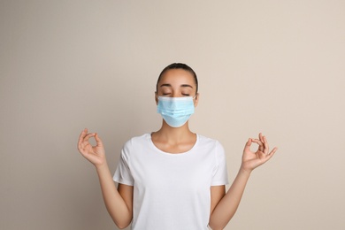 Photo of Woman in protective mask meditating on beige background. Dealing with stress caused by COVID‑19 pandemic