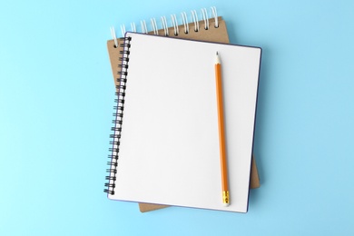 Notebooks with pencil on light blue background, top view