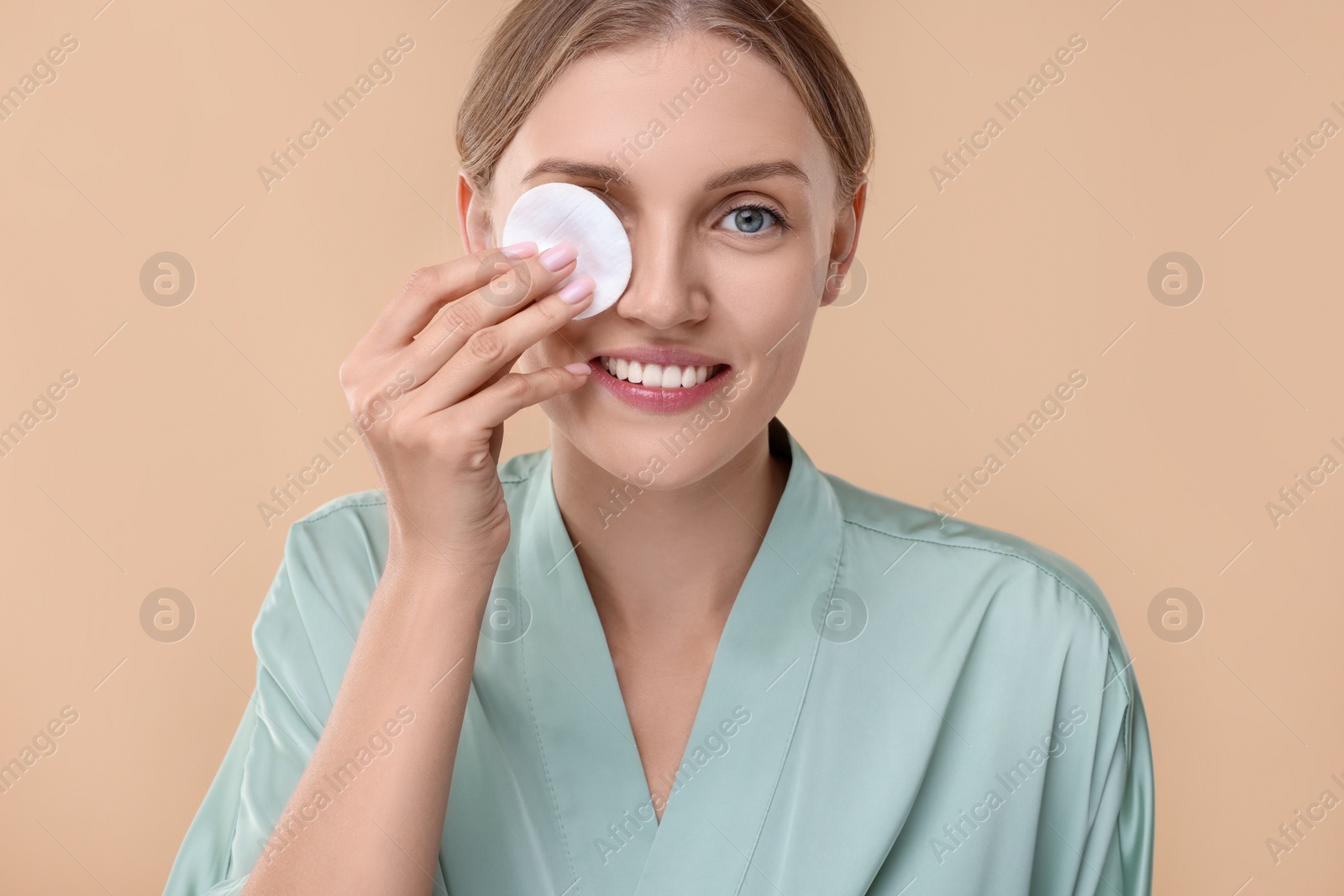 Photo of Young woman cleaning her face with cotton pad on beige background