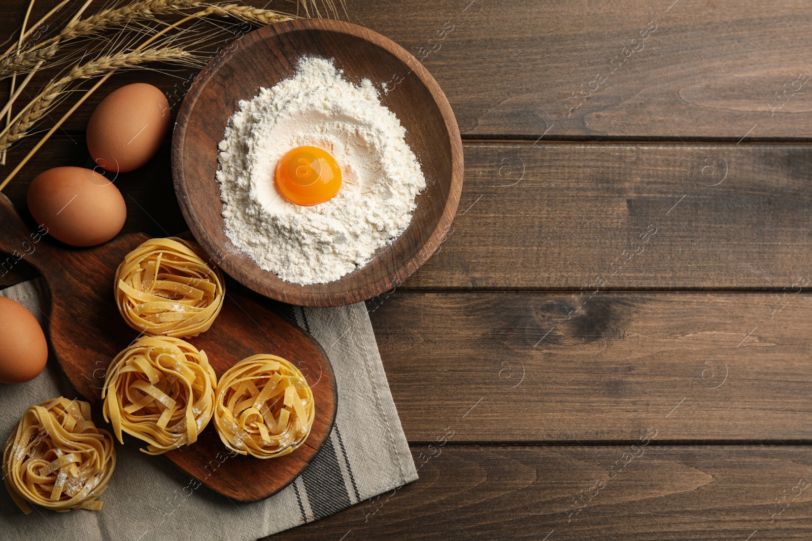 Photo of Flat lay composition with uncooked homemade pasta and ingredients on wooden table. Space for text