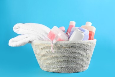 Photo of Wicker basket full of different baby cosmetic products and bathing accessories on light blue background