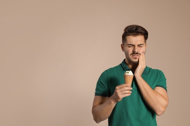 Photo of Emotional young man with sensitive teeth and ice cream on color background. Space for text