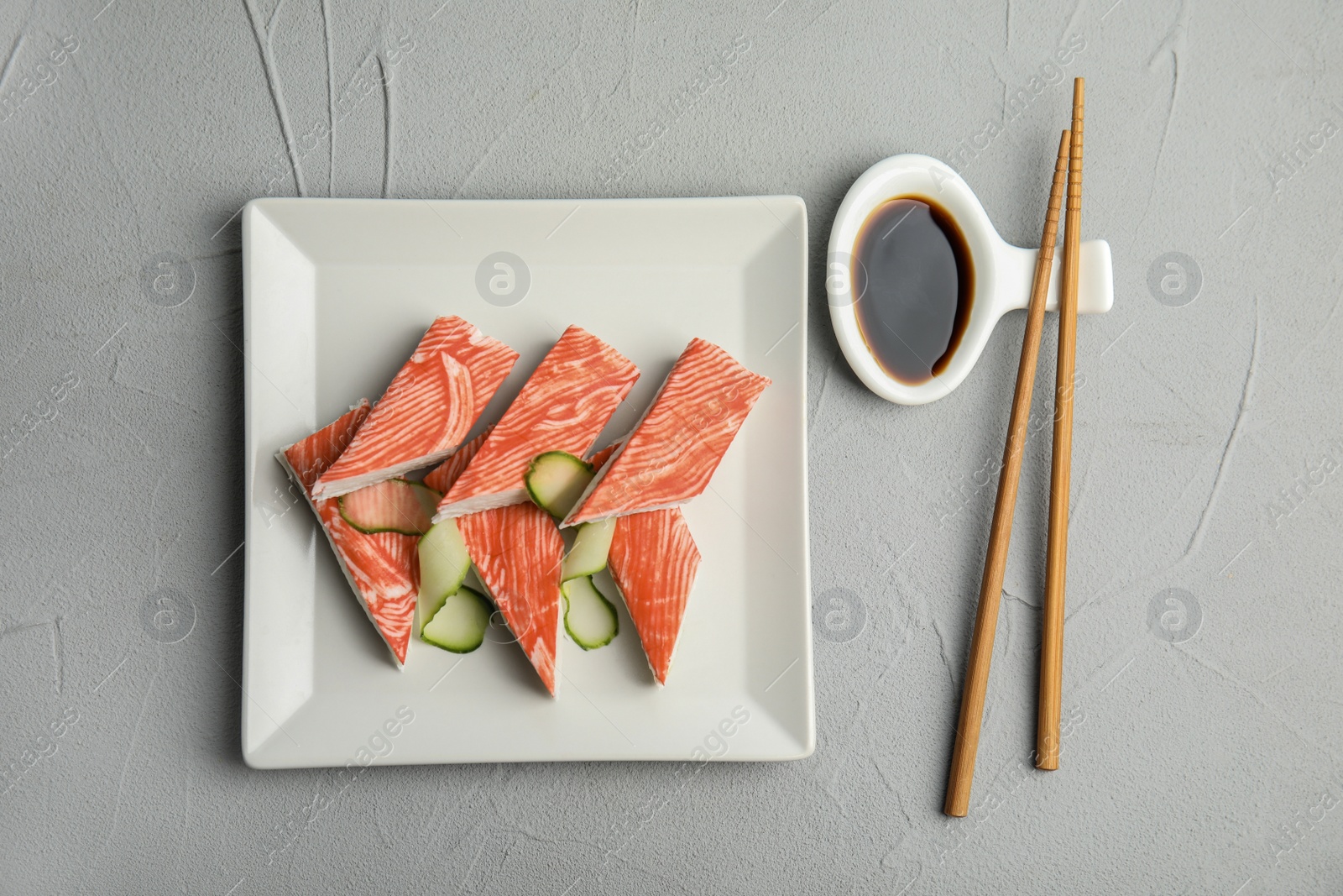 Photo of Fresh crab sticks with cucumber served on grey table, flat lay