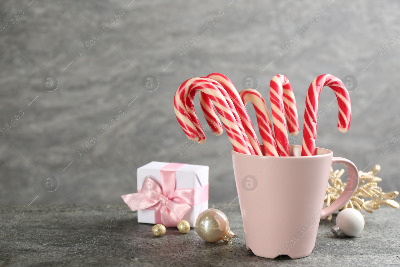 Photo of Candy canes in cup and Christmas decor on grey table, space for text