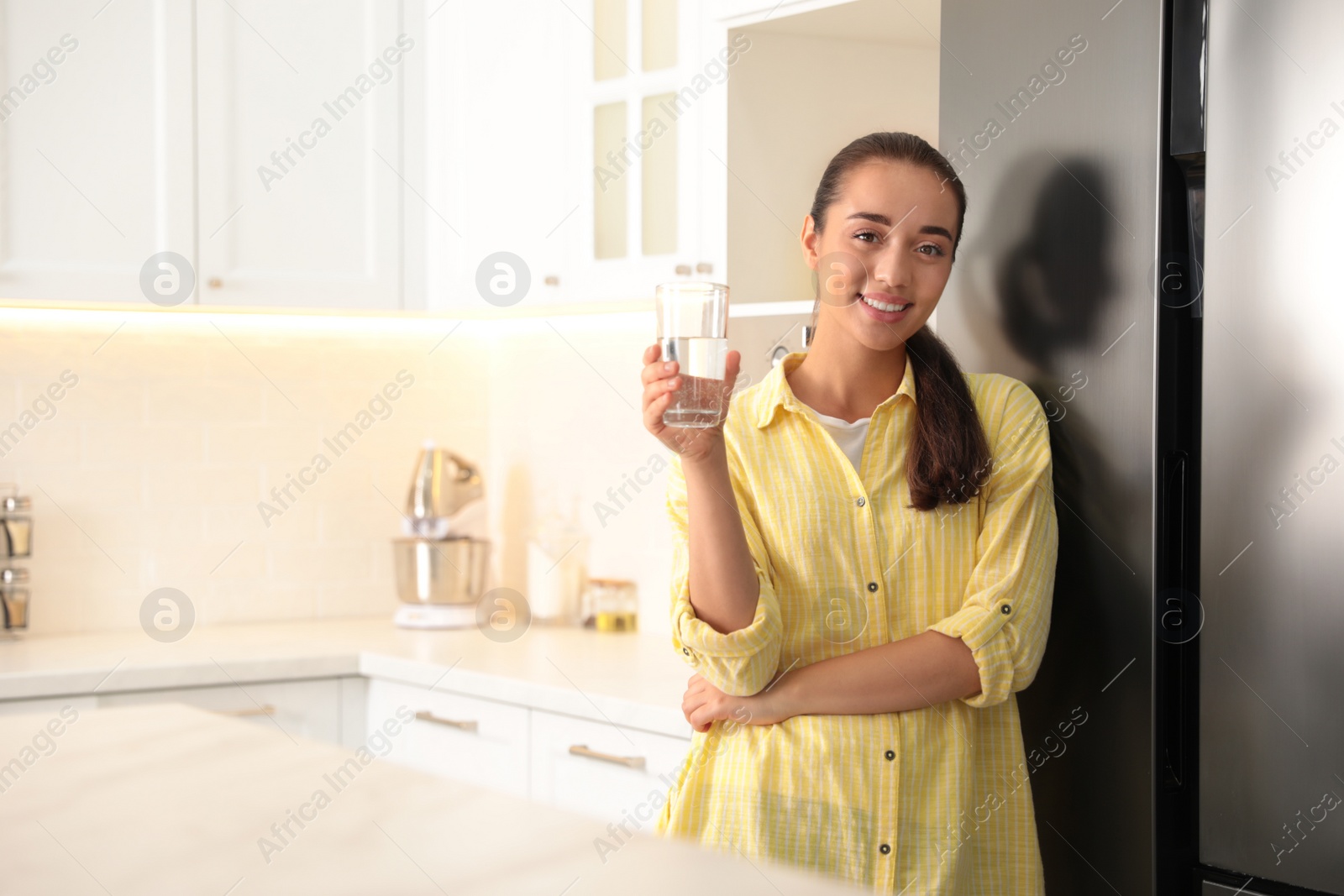 Photo of Young woman holding glass of pure water in kitchen. Space for text