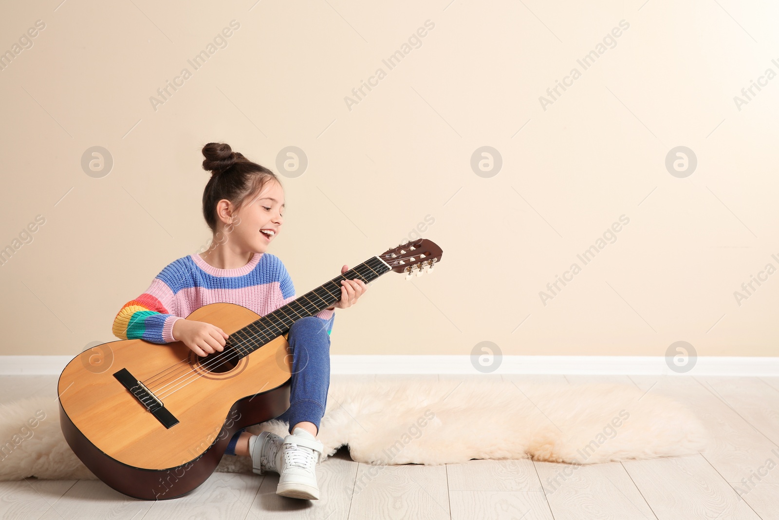 Photo of Cute little girl playing guitar on floor in room. Space for text