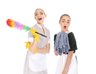 Young chambermaids with dusting brush and mop on white background