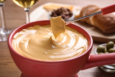 Dipping bread into pot with cheese fondue on table, closeup