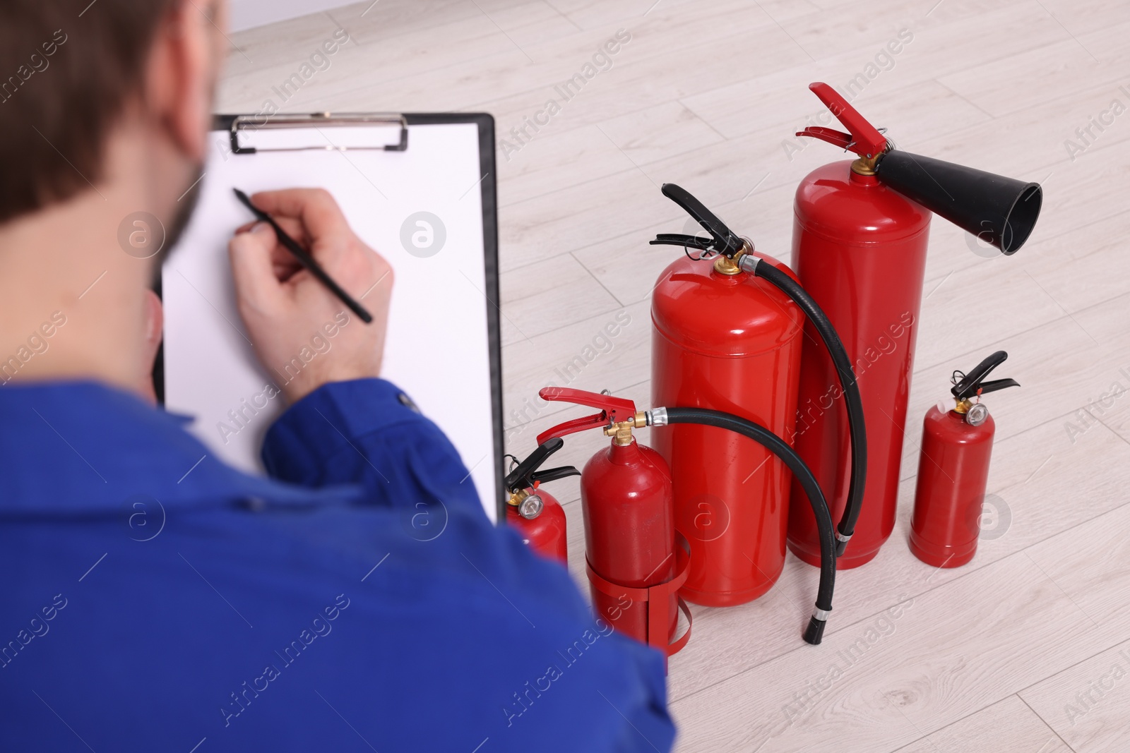 Photo of Man with clipboard checking fire extinguishers indoors, closeup