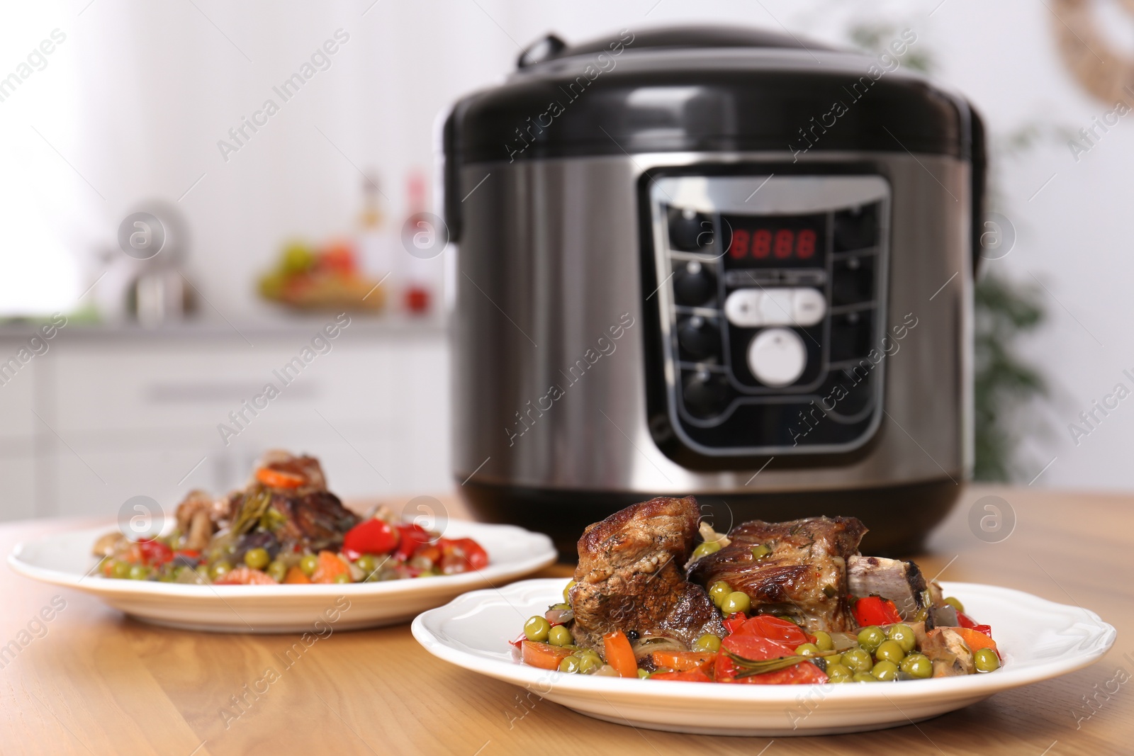 Photo of Plates with meat and garnish prepared in multi cooker on table in kitchen. Space for text