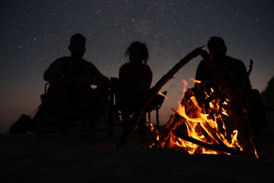 Photo of Group of friends gathering around bonfire in evening, focus on flame. Camping season