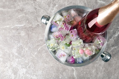 Bottle of champagne with floral ice cubes in bucket on table, top view. Space for text