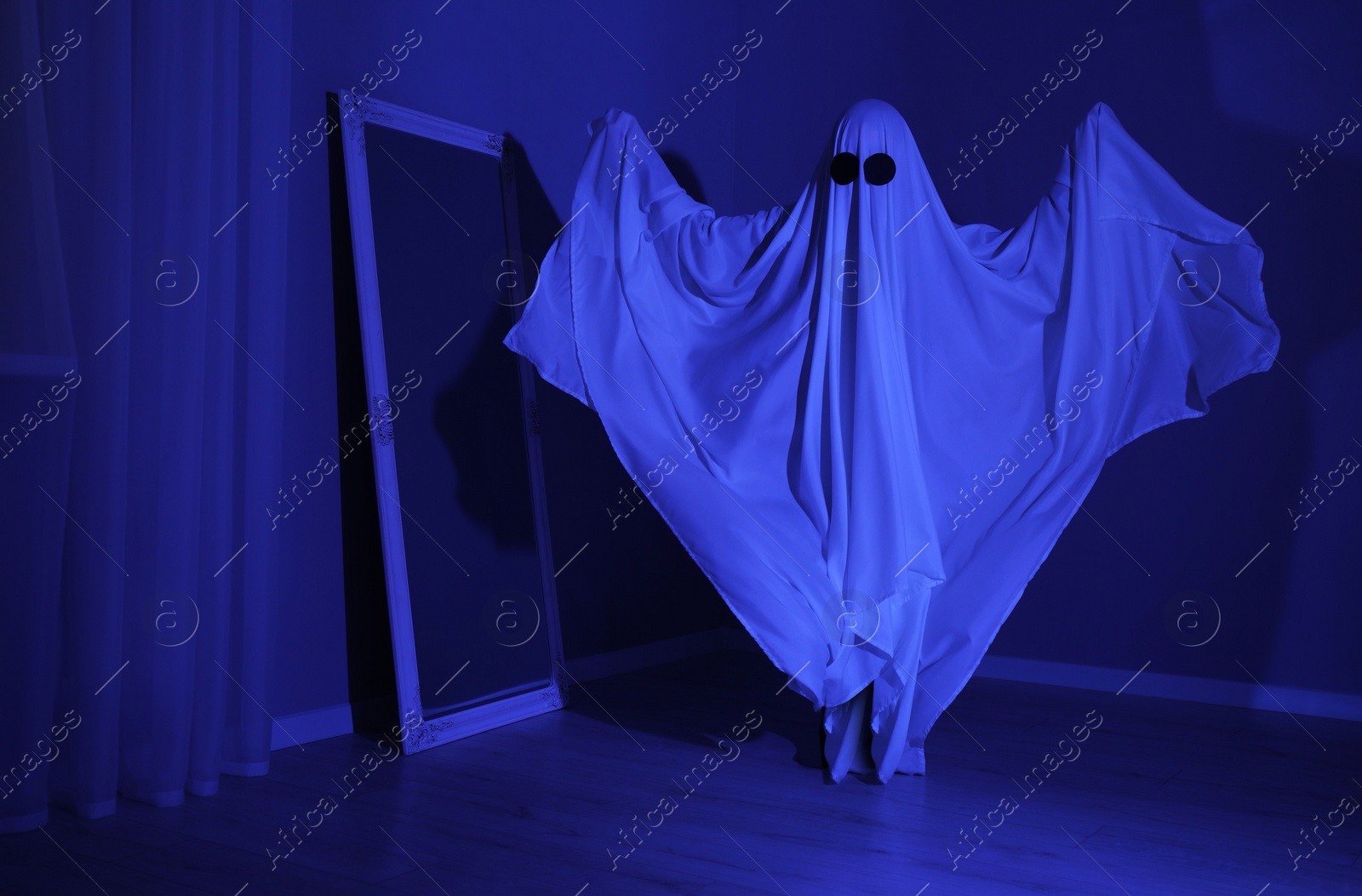 Photo of Creepy ghost. Woman covered with sheet in blue light