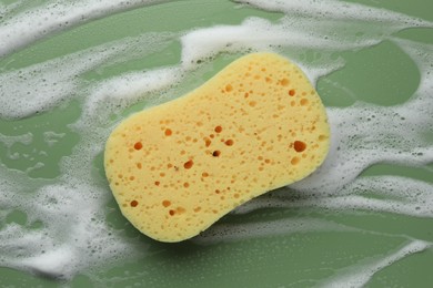 Yellow sponge with foam on green background, top view