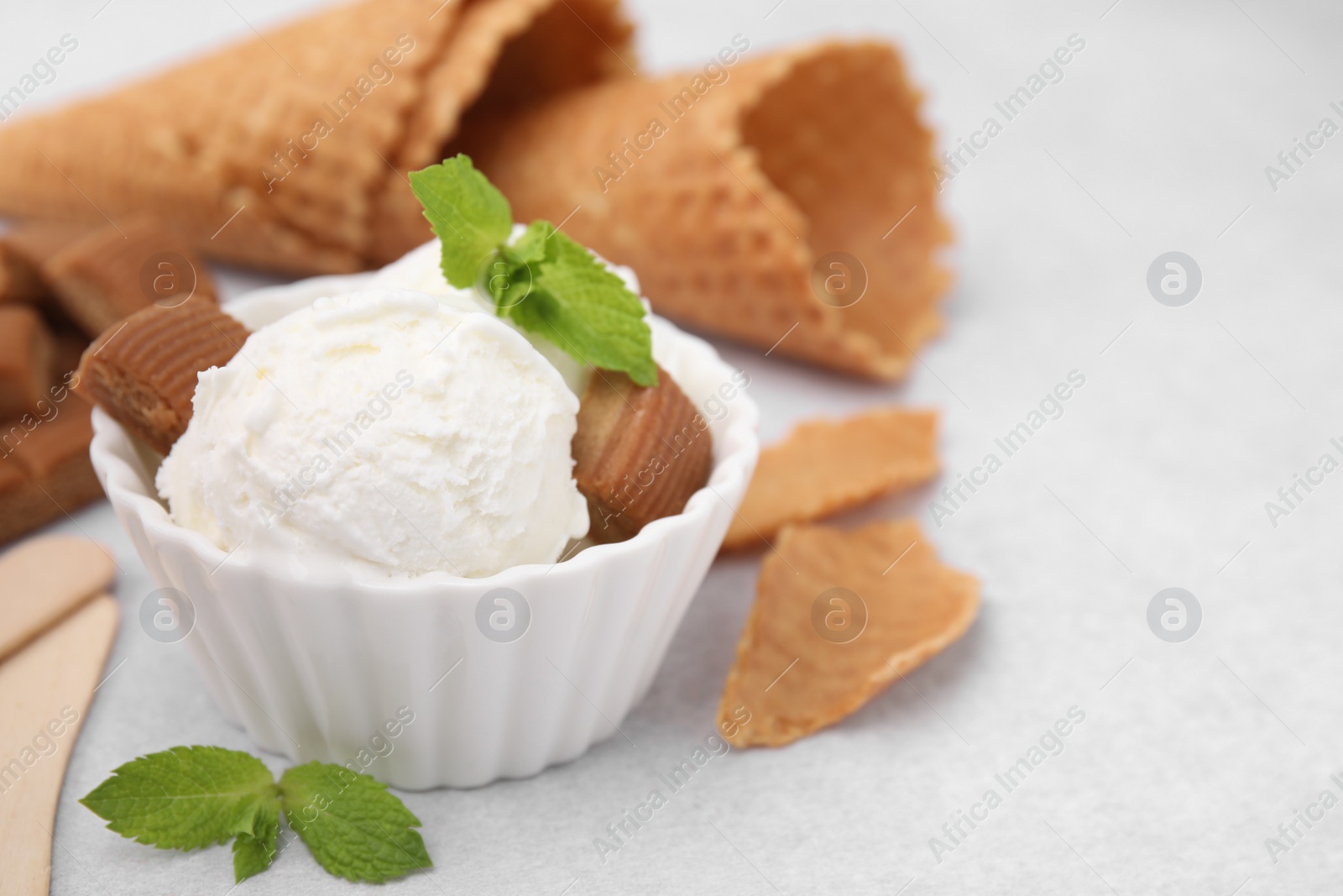 Photo of Scoops of tasty ice cream with mint leaves and caramel candies on white table, closeup. Space for text
