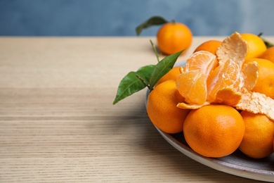 Photo of Plate with fresh ripe tangerines on wooden table. Space for text