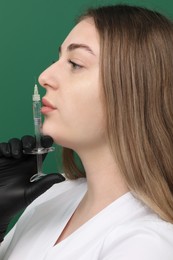 Cosmetologist with syringe on green background, closeup