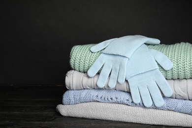 Photo of Stacked sweaters and gloves on table, closeup with space for text. Autumn clothes