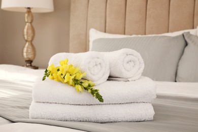 Photo of Fresh white towels with flower on bed indoors