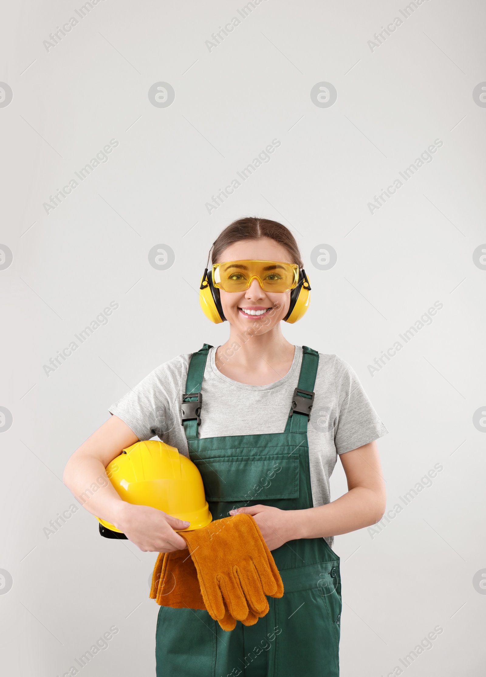 Photo of Female industrial worker in uniform on light background. Safety equipment