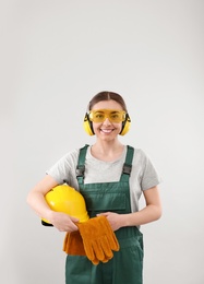 Photo of Female industrial worker in uniform on light background. Safety equipment