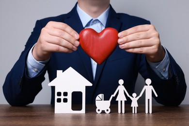 Photo of Man holding figure of heart above family at wooden table. closeup. Insurance concept