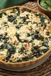 Photo of Delicious homemade spinach quiche on wicker mat, closeup