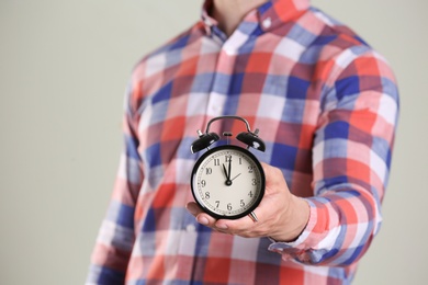 Young man holding alarm clock on grey background. Time concept