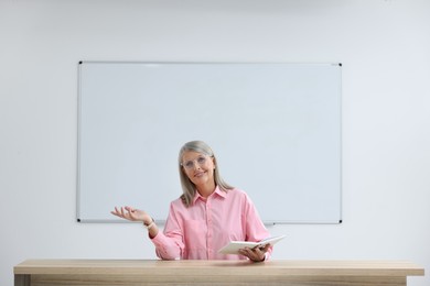 Photo of Happy professor with book giving lecture at desk in classroom