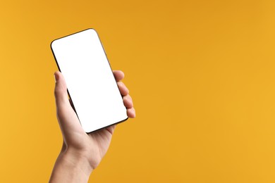 Photo of Man holding smartphone with blank screen on yellow background, closeup. Mockup for design