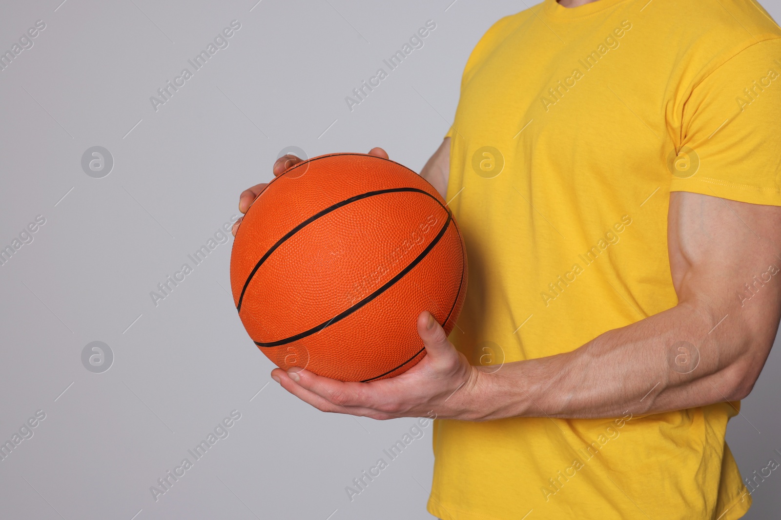 Photo of Athletic young man with basketball ball on light grey background, closeup